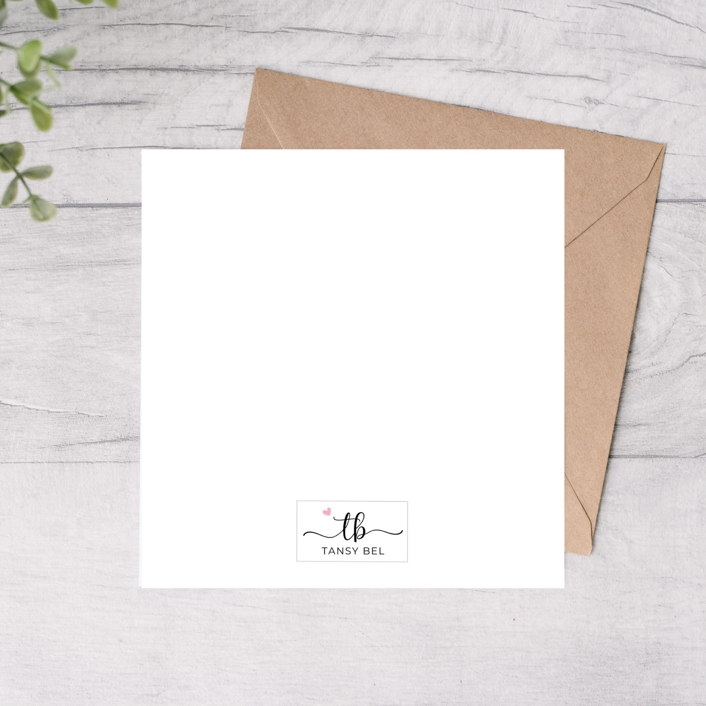 White card with a brown envelope on a light wooden surface, featuring the brand 'Tansy Bel'.
