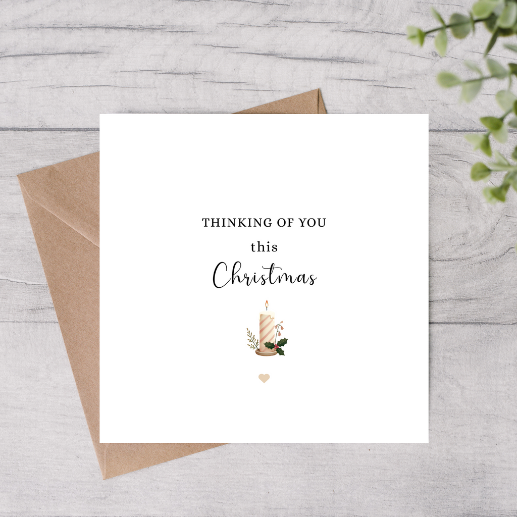 Greeting card with 'Thinking of you this Christmas' text and a candle illustration on a wooden surface.