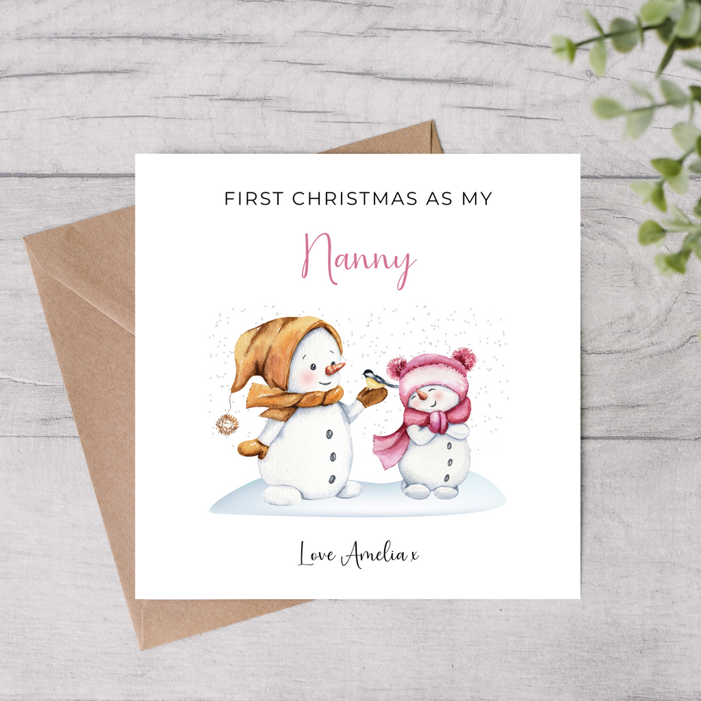 Greeting card with snowman and baby illustration for 'First Christmas as my Nanny' on a wooden surface.