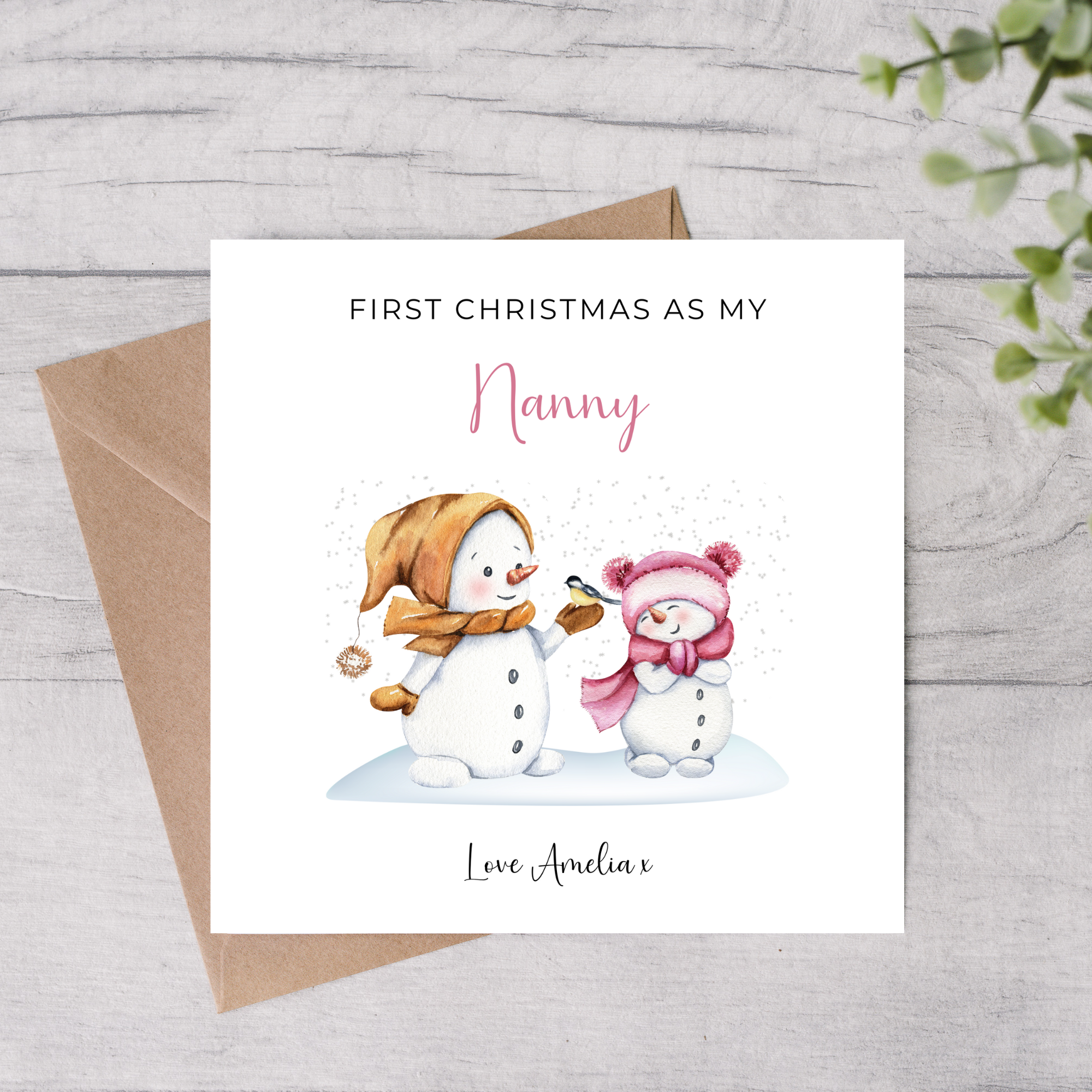 Greeting card with snowman and baby illustration for 'First Christmas as my Nanny' on a wooden surface.
