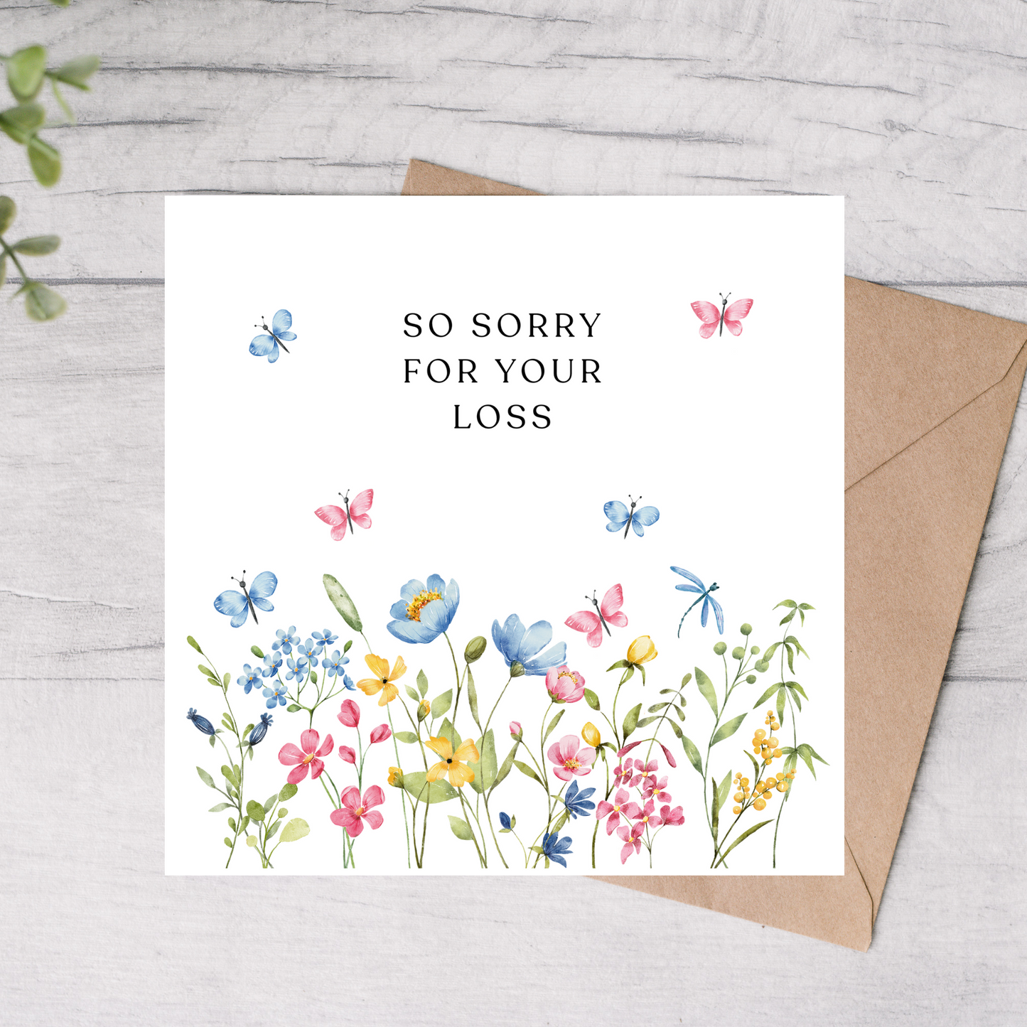 Greeting card with floral design and 'So sorry for your loss' text on a wooden surface.