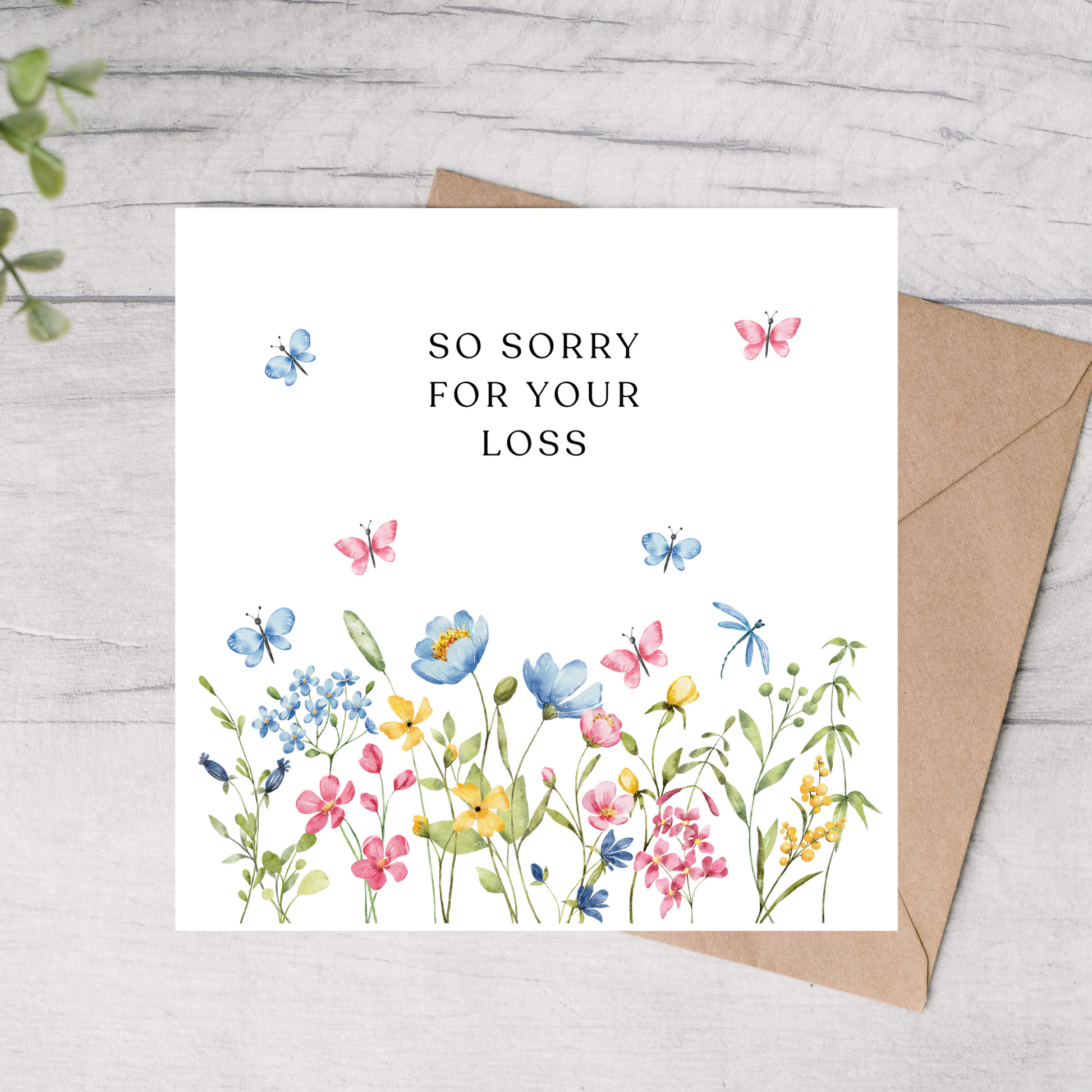 Greeting card with floral design and 'So sorry for your loss' text on a wooden surface.