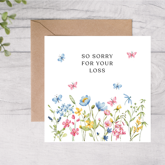 Greeting card with floral design and 'So sorry for your loss' text on a wooden surface.
