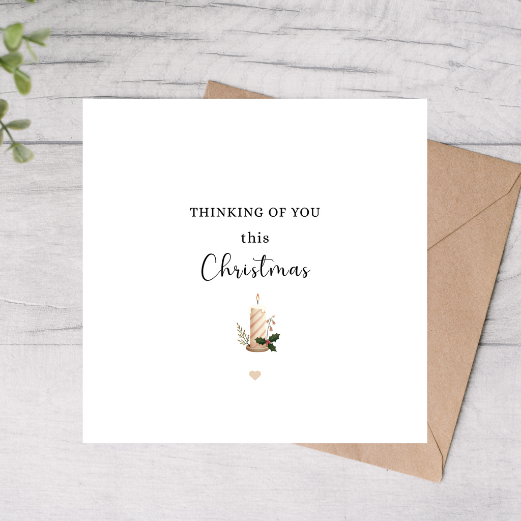 Greeting card with 'Thinking of you this Christmas' text and a candle illustration, placed on a wooden surface.