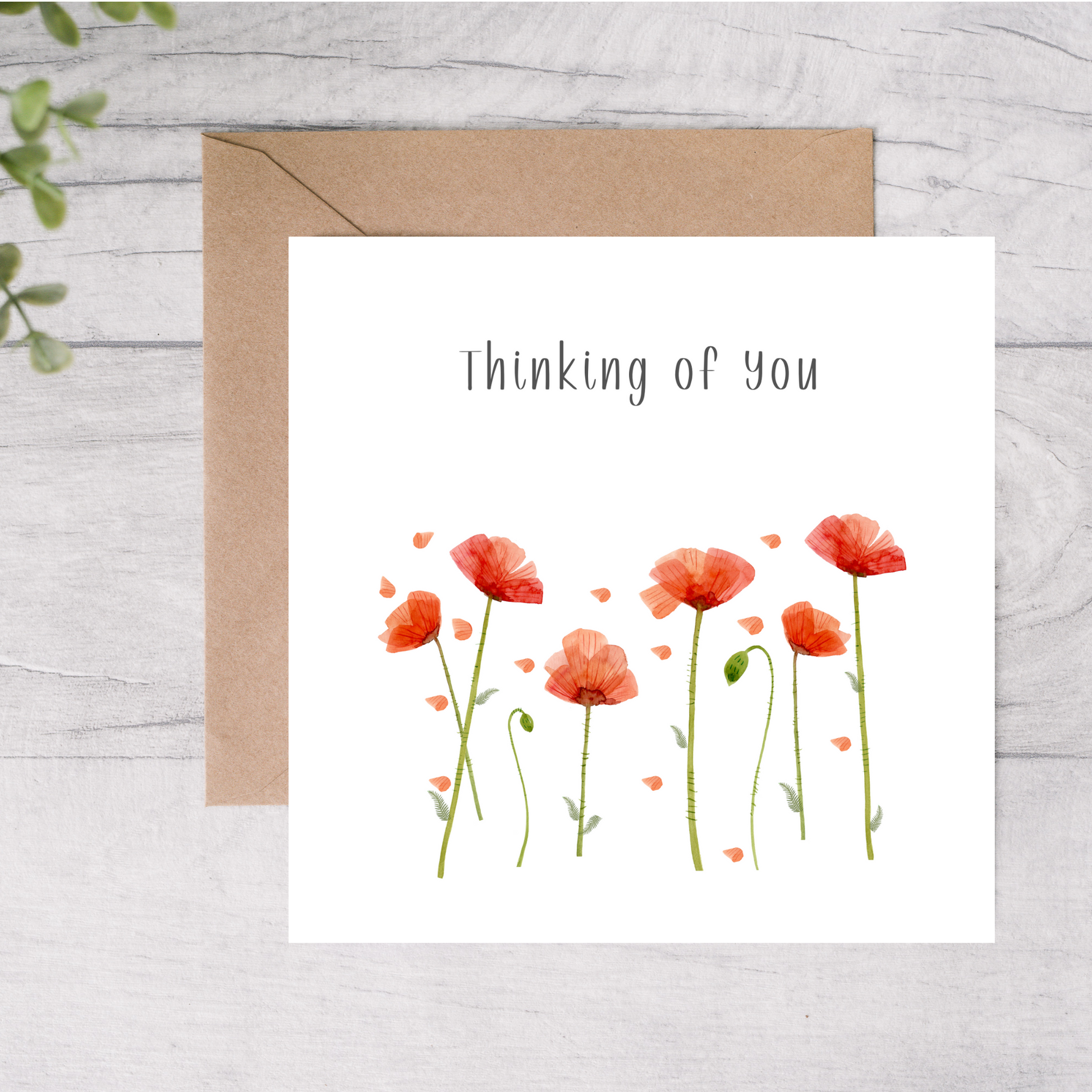 Greeting card with poppy flowers and 'Thinking of you' text on a wooden surface.
