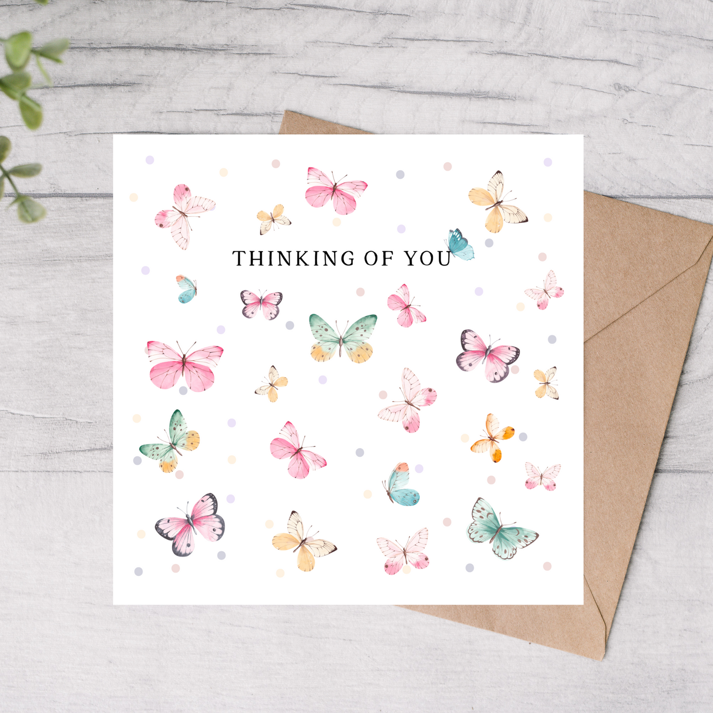 Greeting card with colorful butterflies and 'Thinking of You' text on a white background with a brown envelope.