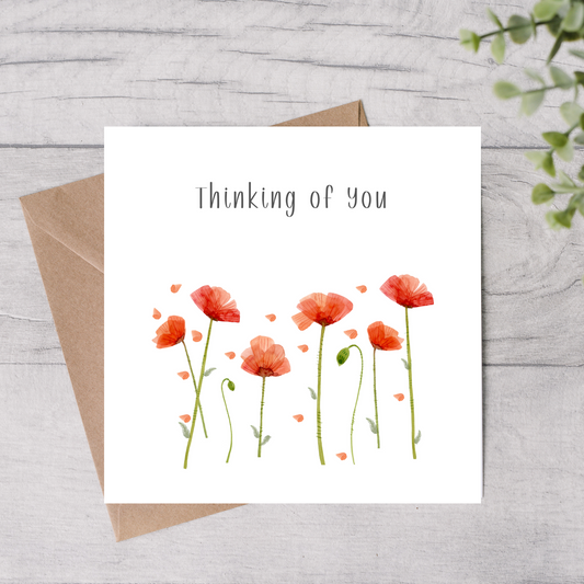Greeting card with red flowers and 'Thinking of You' text on a wooden surface