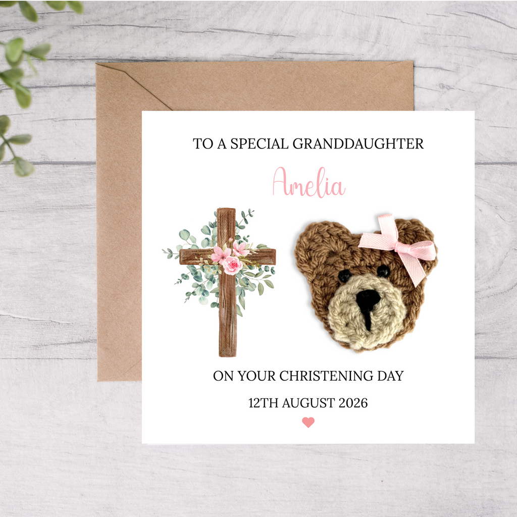 Personalized christening card with teddy bear and cross design on a wooden surface.