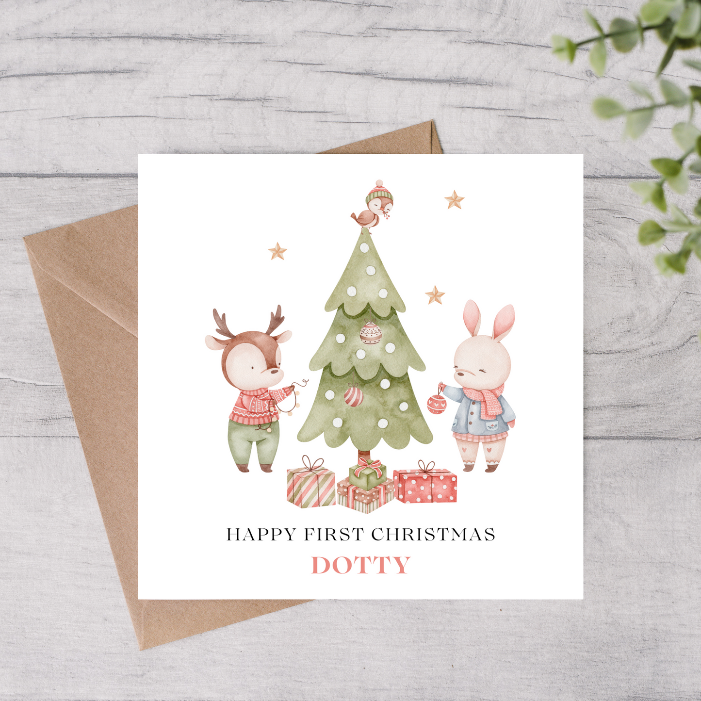 1st Christmas card with a deer and rabbit by a decorated tree, on a wooden surface.