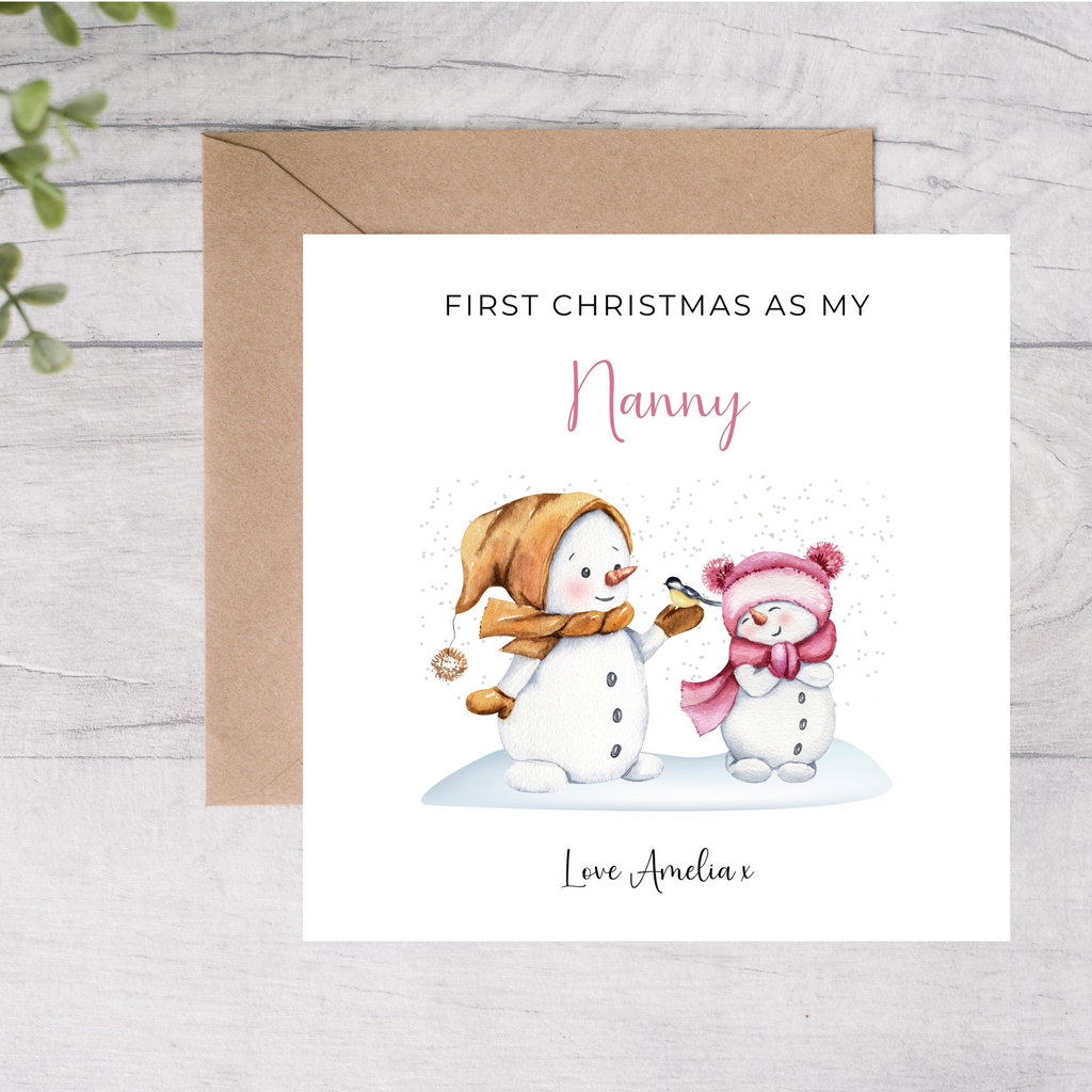 Card with snowman and baby illustration and text 'First Christmas as my Nanny' on a wooden surface.