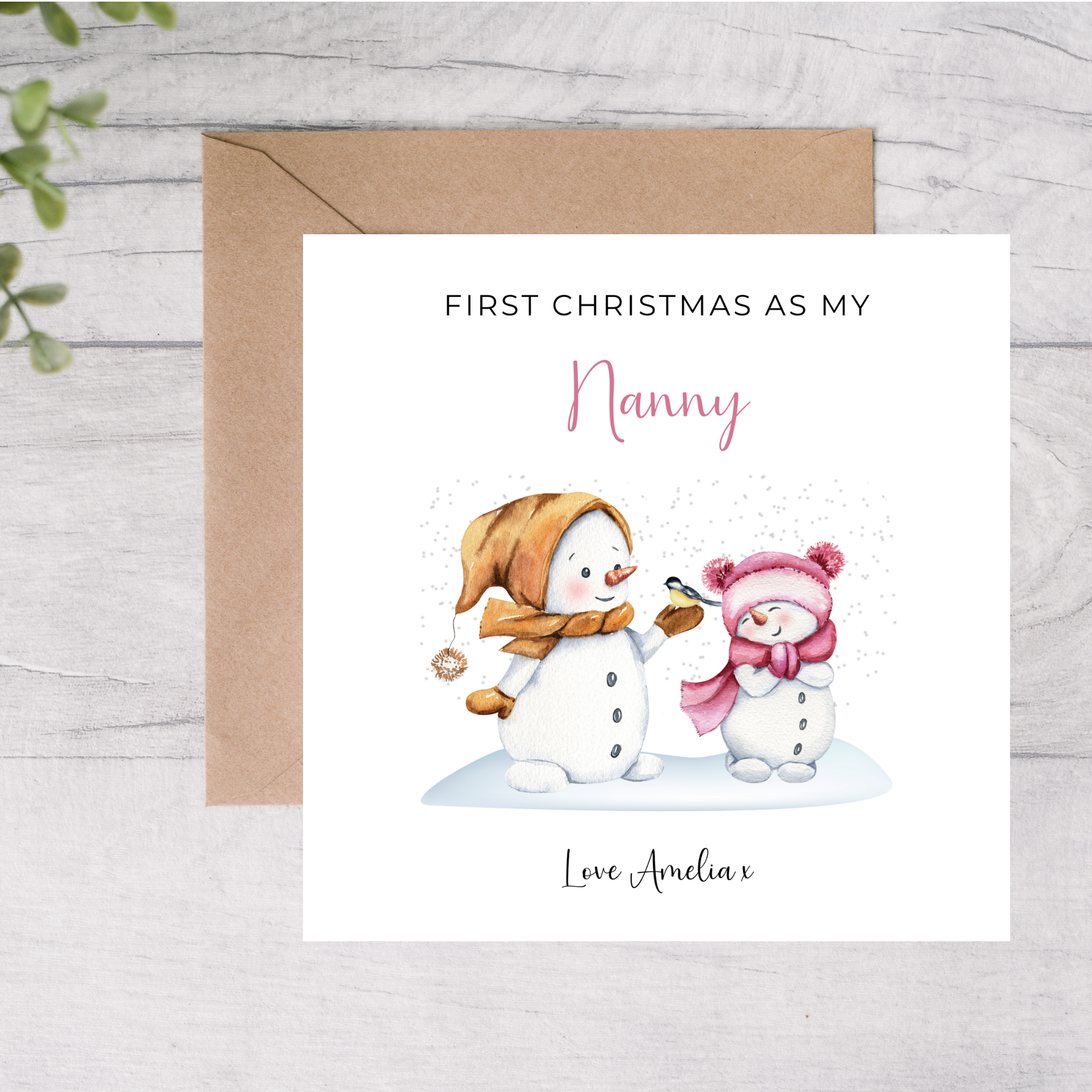 Card with snowman and baby illustration and text 'First Christmas as my Nanny' on a wooden surface.
