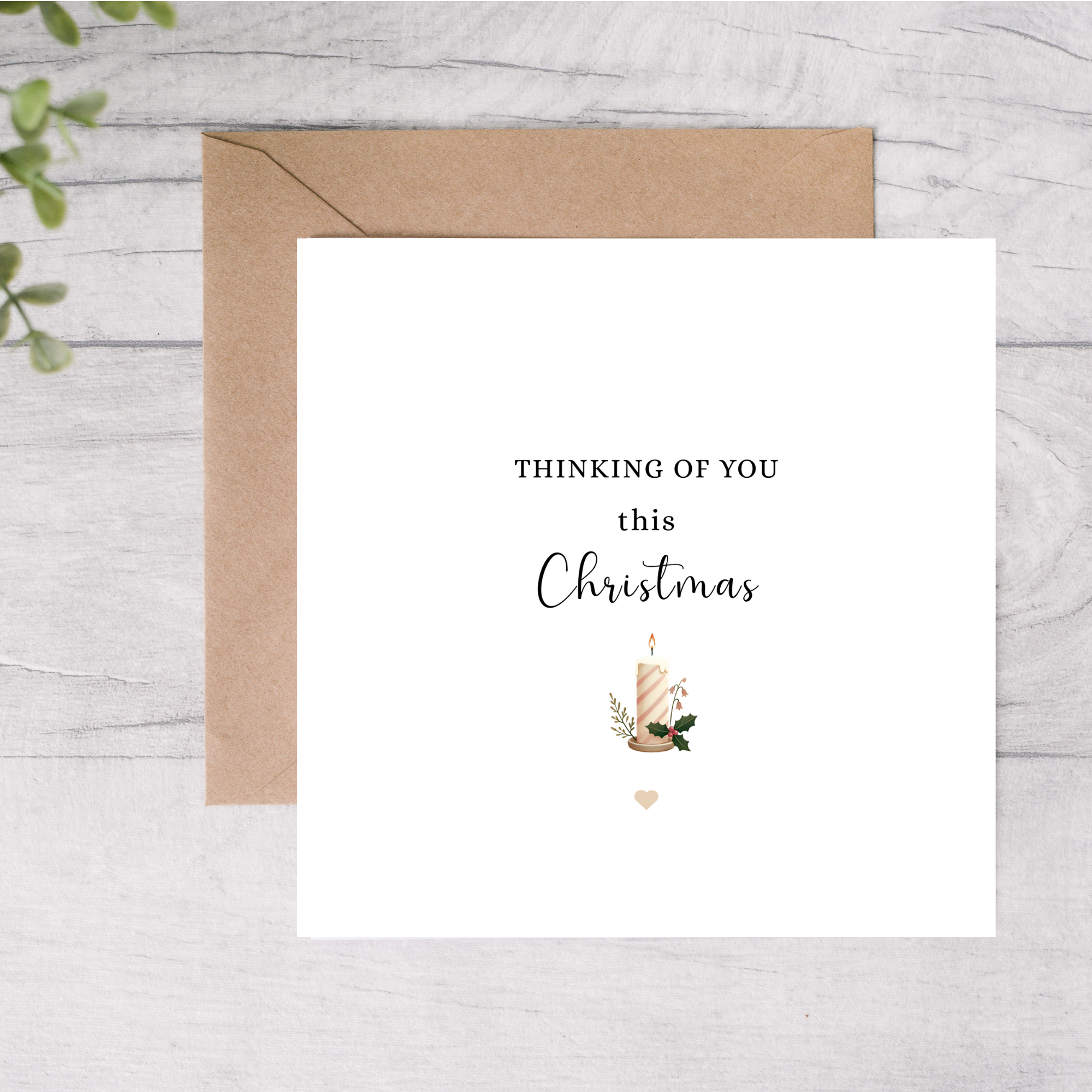Greeting card with 'Thinking of you this Christmas' text and a candle illustration on a wooden surface.