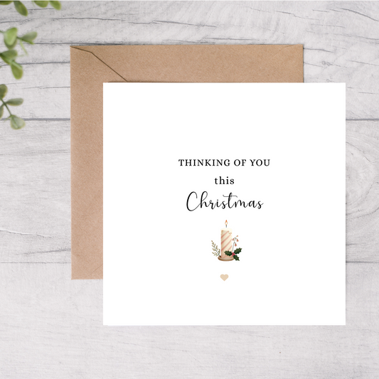 Greeting card with 'Thinking of you this Christmas' text and a candle illustration on a wooden surface.